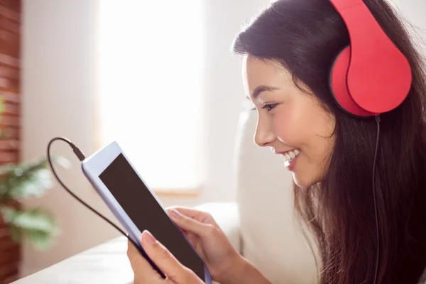 Sorrindo mulher asiática no sofá ouvindo música — Fotografia de Stock