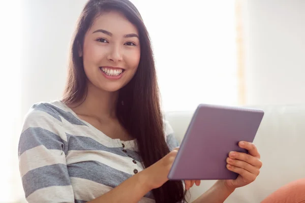 Smiling asian woman using tablet on couch — Stock Photo, Image