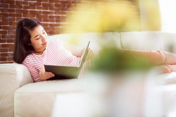 Sonriendo asiático mujer en sofá lectura — Foto de Stock