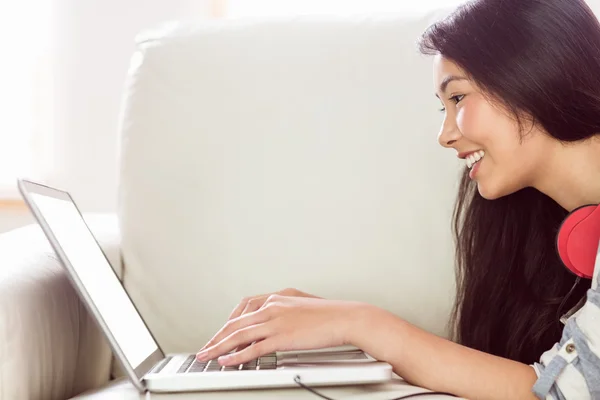 Lächelnde asiatische Frau auf der Couch mit Laptop — Stockfoto