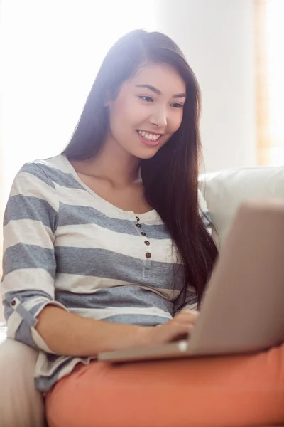 Sorridente donna asiatica utilizzando il computer portatile sul divano — Foto Stock