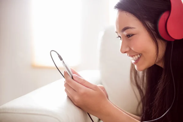 Sorridente donna asiatica sul divano ad ascoltare musica — Foto Stock