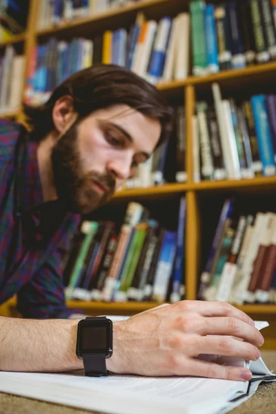 Студент, який навчається на підлозі в бібліотеці, носить розумний годинник — стокове фото