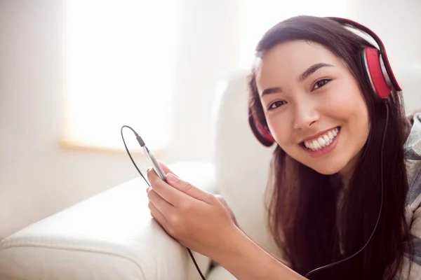 Sorrindo mulher asiática no sofá ouvindo música — Fotografia de Stock