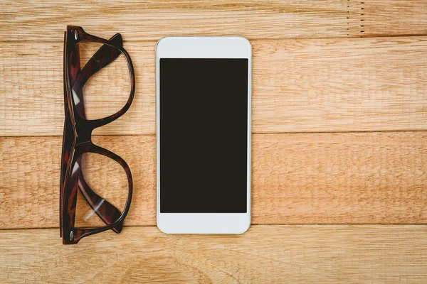 Óculos e um smartphone na mesa de madeira — Fotografia de Stock