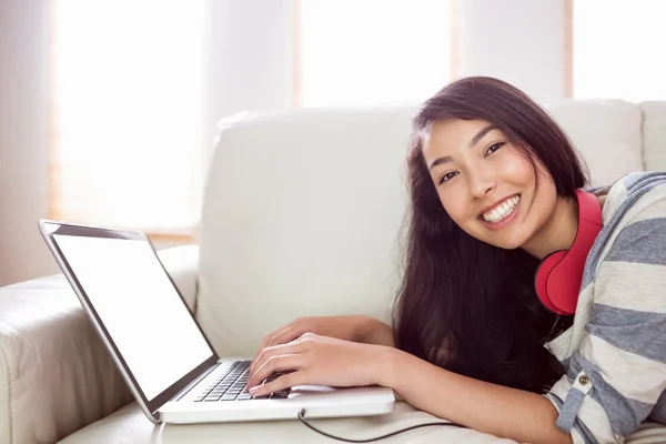Smiling asian woman on couch using laptop — Stock Photo, Image