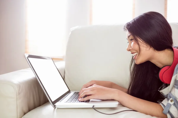 Smiling asian woman on couch using laptop — Stock Photo, Image