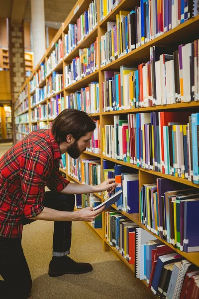 Étudiant ramassant un livre dans une étagère de la bibliothèque — Photo