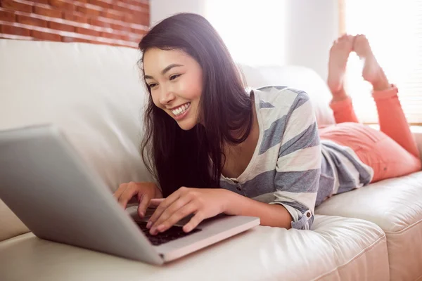 Souriant asiatique femme sur canapé en utilisant un ordinateur portable — Photo