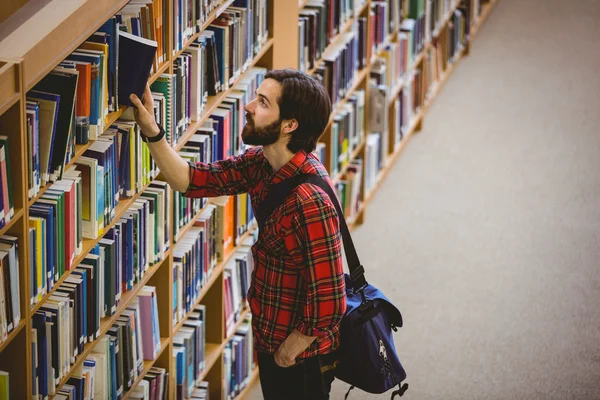 Estudiante recogiendo un libro de un estante en la biblioteca — Foto de Stock