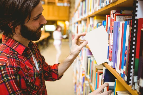 Hipster student plocka en bok i biblioteket — Stockfoto