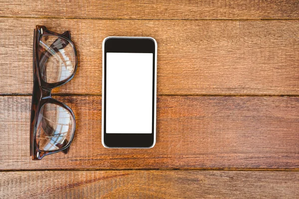 Óculos e um smartphone na mesa de madeira — Fotografia de Stock