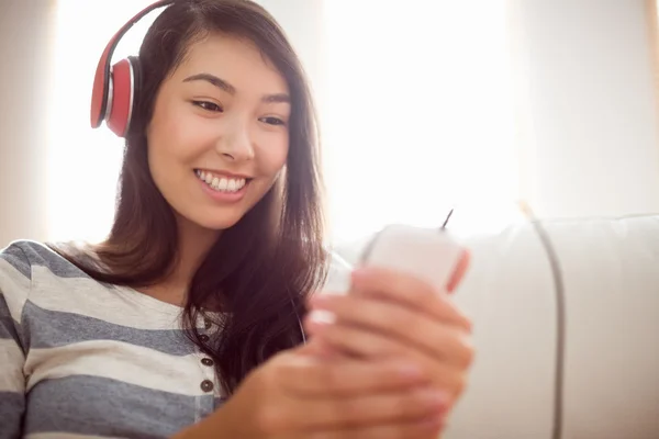 Улыбающаяся азиатка на диване слушает музыку — стоковое фото