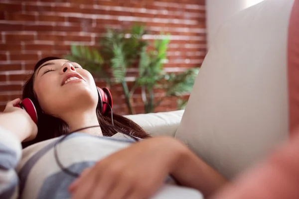 Sorridente donna asiatica sul divano ad ascoltare musica — Foto Stock