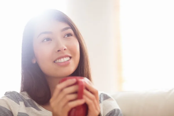 Sorridente donna asiatica sul divano avendo bevanda calda — Foto Stock