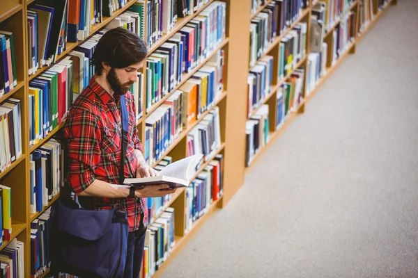 Estudante lendo um livro de prateleira na biblioteca — Fotografia de Stock