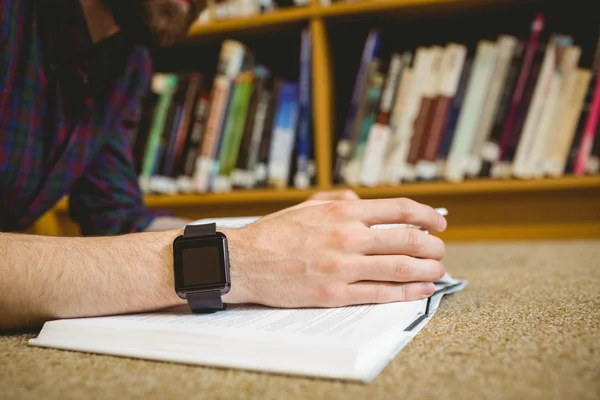 Étudiant étudiant sur le sol en bibliothèque portant une montre intelligente — Photo