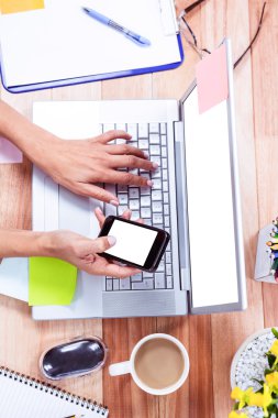 Overhead of feminine hands using laptop and smartphone clipart