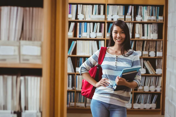 Bella studentessa in piedi in biblioteca con un libro in mano — Foto Stock