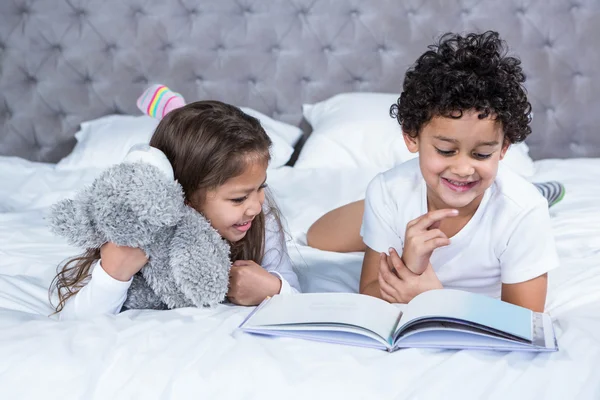 Милый брат и сестра читают книгу на кровати — стоковое фото