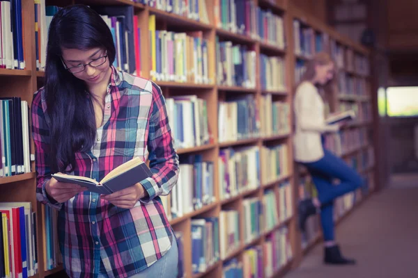 Lachende student leunend tegen boekenkasten lezen van boek — Stockfoto