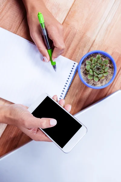 Vrouwelijke handen met smartphone en maken van aantekeningen — Stockfoto