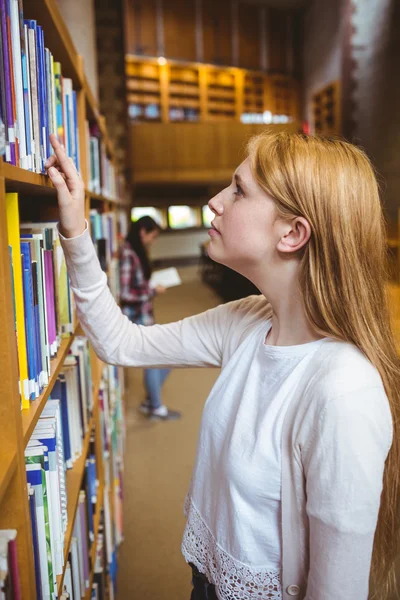 Blonde Studentin sucht Buch in Bücherregalen — Stockfoto