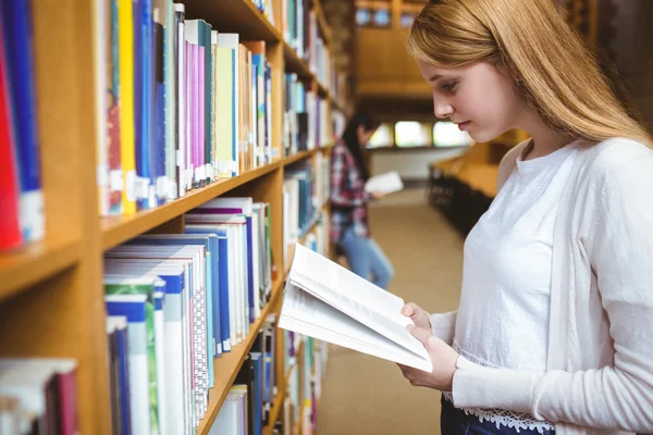 Estudante loira lendo livro na biblioteca — Fotografia de Stock