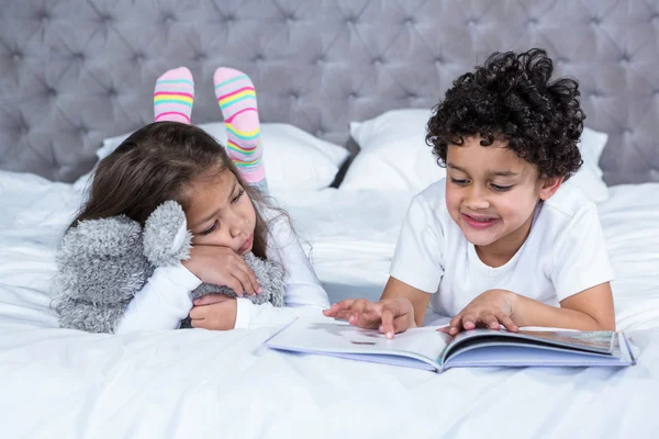 Симпатичные братья и сестры читают книгу на кровати — стоковое фото