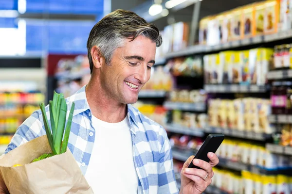 Улыбающийся мужчина с продуктовой сумкой с помощью смартфона — стоковое фото