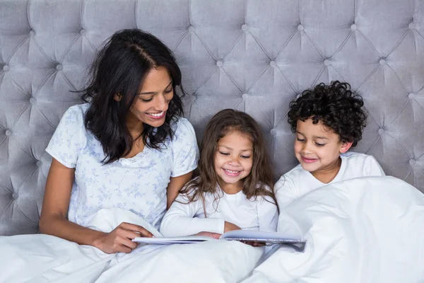 Happy family reading book on the bed — Stock Photo, Image