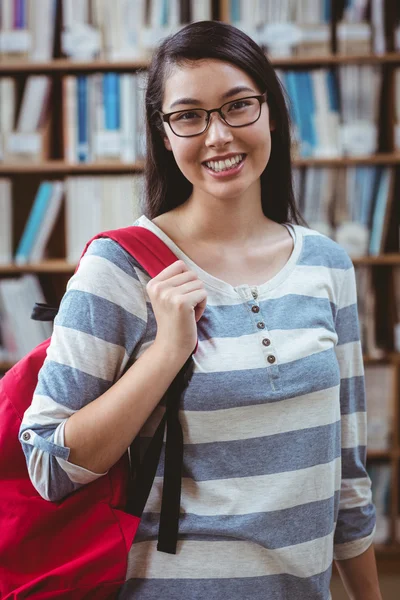 Estudante sorridente com mochila em pé na biblioteca — Fotografia de Stock