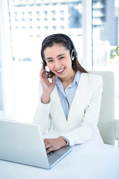 Donna d'affari sorridente con auricolare utilizzando il computer portatile — Foto Stock