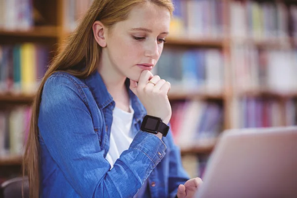 Estudiante con smartwatch usando laptop en la biblioteca —  Fotos de Stock