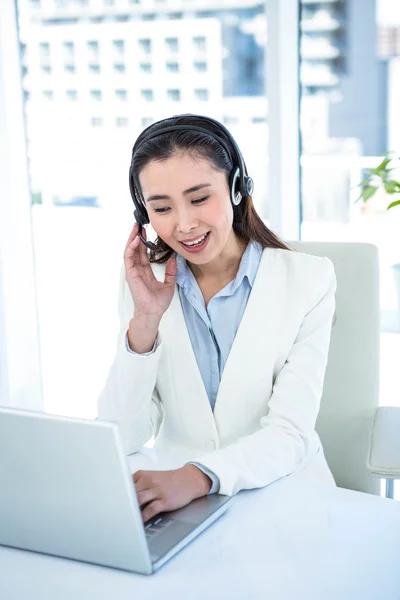 Donna d'affari sorridente con auricolare utilizzando il computer portatile — Foto Stock