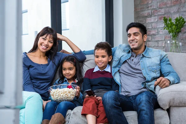 Feliz familia joven comiendo palomitas de maíz mientras ve la televisión —  Fotos de Stock