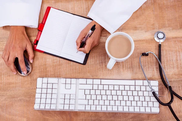 Doctor usando el ratón y la escritura en el diario — Foto de Stock