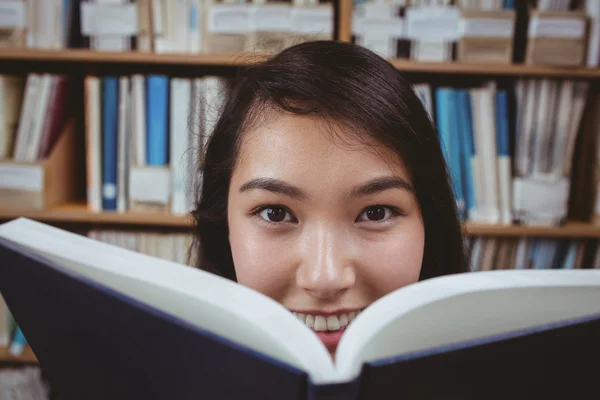 Smiling student hiding face behind a book — Stock Photo, Image