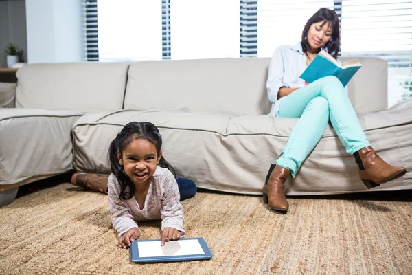 Glad mamma läsa bok medan hennes dotter använder tablet — Stockfoto