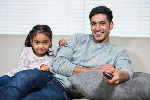 Улыбающийся отец смотрит телевизор с дочерью на диване — стоковое фото