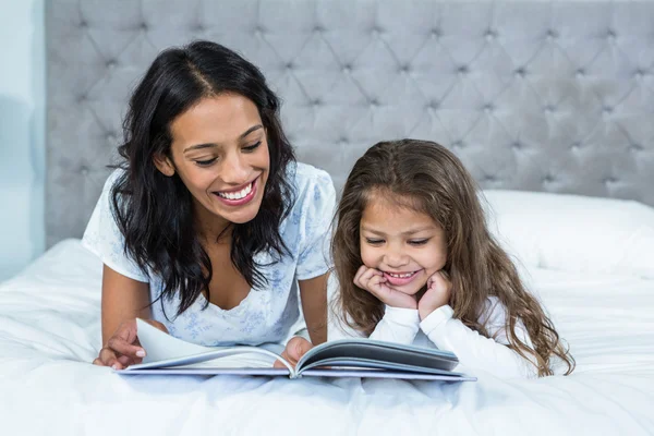 Счастливые мать и дочь читают книгу на кровати — стоковое фото