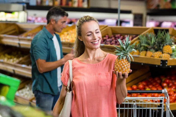 Sorrindo mulher segurando e olhando um abacaxi — Fotografia de Stock