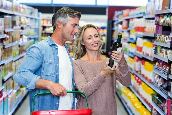 Pareja sonriente mirando una botella de vino — Foto de Stock