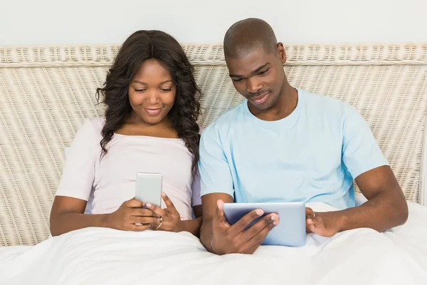 Pareja relajada usando tecnología en la cama —  Fotos de Stock