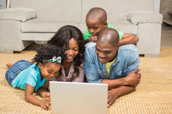 Família feliz deitada no chão usando laptop — Fotografia de Stock