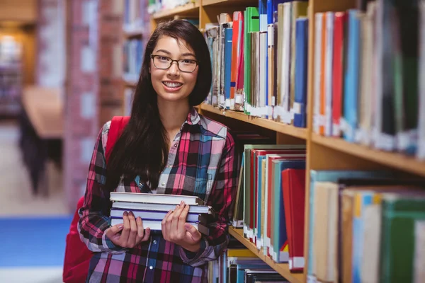 Χαμογελώντας φοιτητής εκμετάλλευση βιβλία στη βιβλιοθήκη — Φωτογραφία Αρχείου