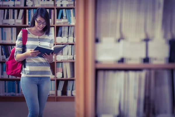 Graziosa studentessa con zaino che legge un libro in biblioteca — Foto Stock