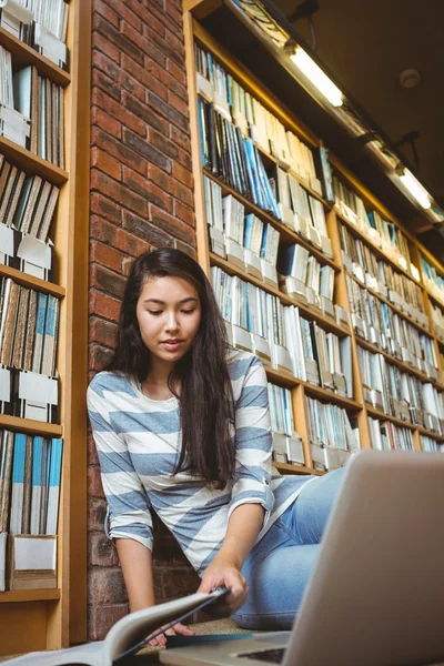 Leende student sitter på golvet mot vägg i biblioteket stu — Stockfoto