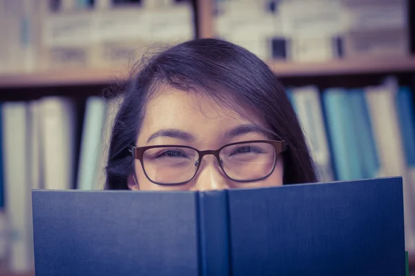 Estudante bonito escondendo o rosto atrás de um livro — Fotografia de Stock