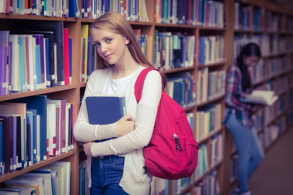 Smiling student leaning against bookshelves — Stock Photo, Image